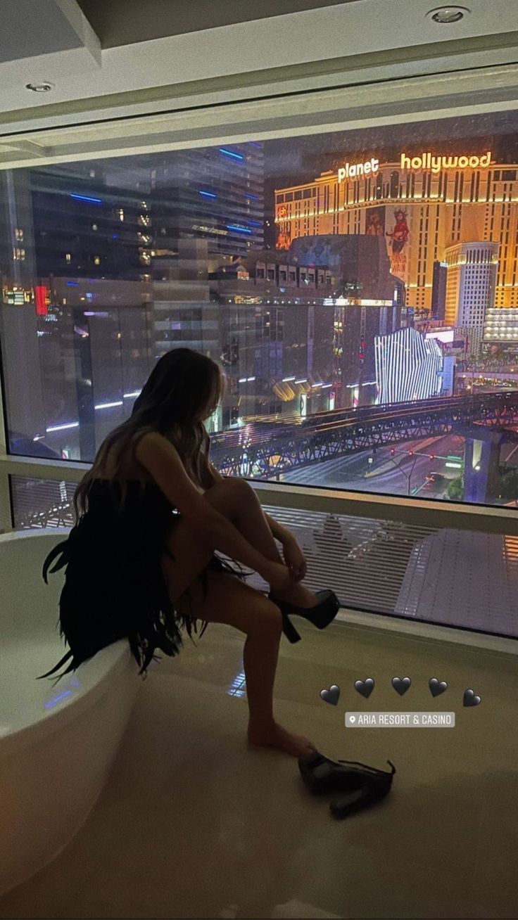 a woman sitting in a bathtub looking out at the las vegas strip