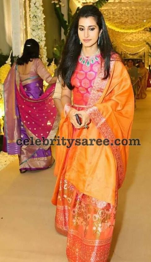 a woman in an orange and pink sari walking down a hall with other women