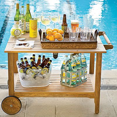 an outdoor bar cart with bottles and glasses on it next to a pool filled with water