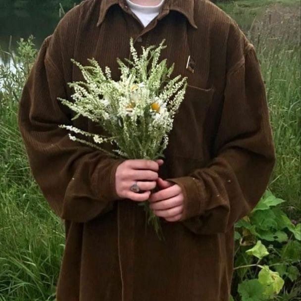 a man standing in front of a body of water holding a bouquet of white flowers