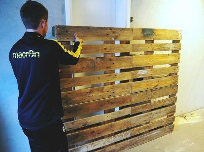 a man standing next to a wooden wall made out of pallets and wood planks