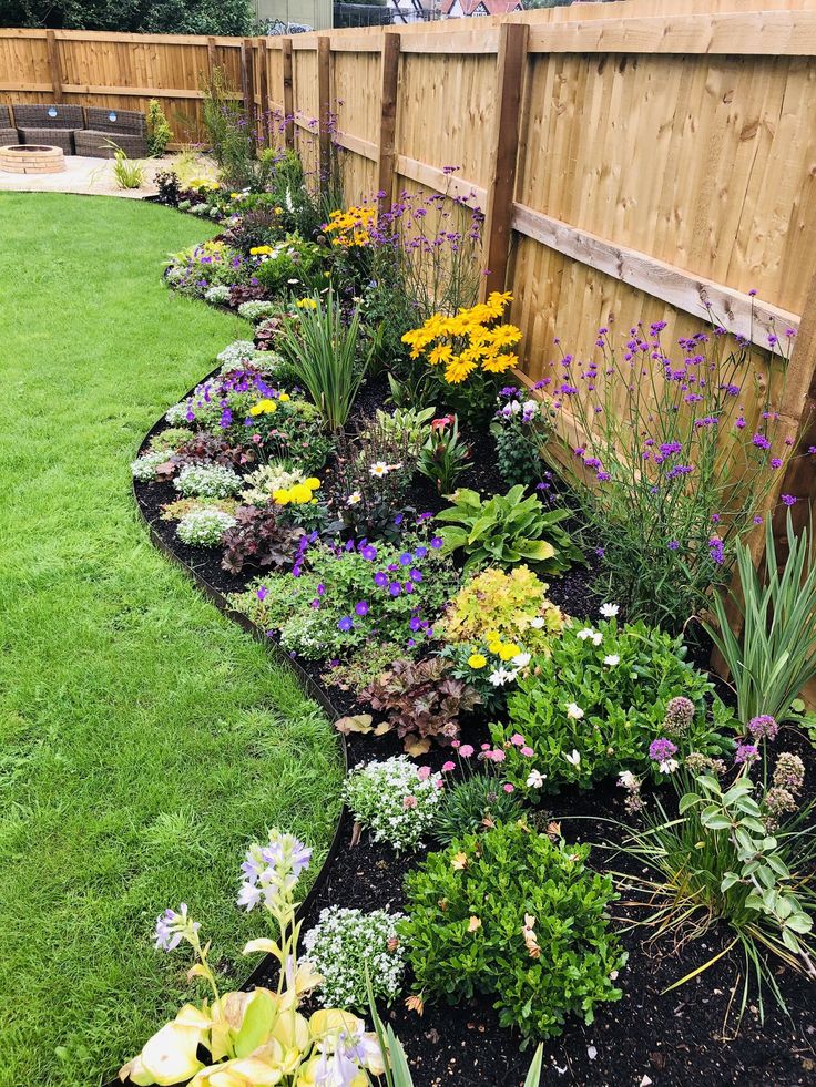 a garden filled with lots of flowers next to a wooden fence on top of grass