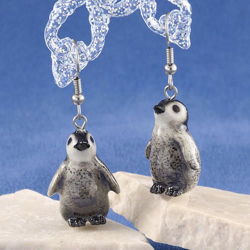 pair of penguin earrings with swaroons on white rock against blue background, closeup