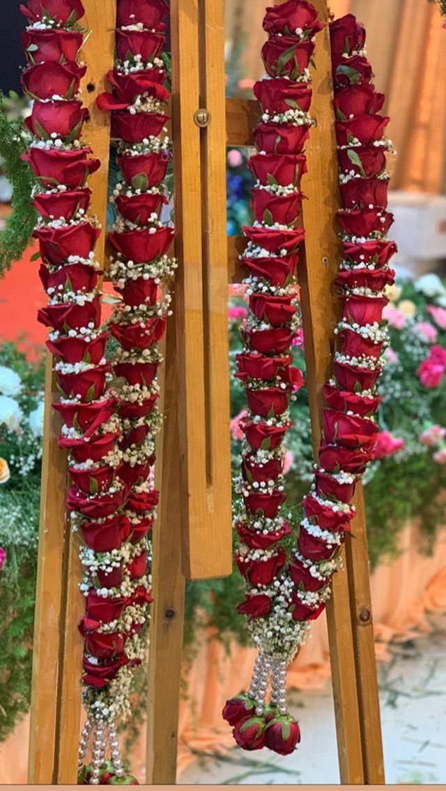 red roses and pearls are arranged on a wooden easel in front of pink flowers