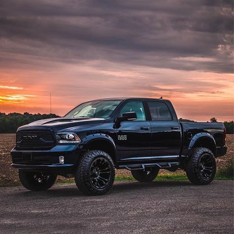 a black truck parked on top of a dirt road next to a field at sunset