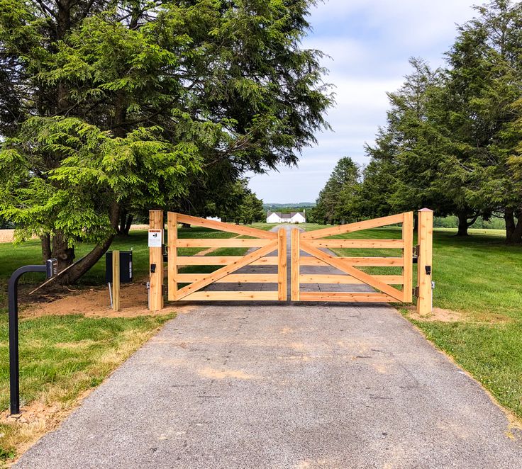 a wooden gate in the middle of a grassy area with trees and grass around it