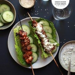 a plate with cucumber and chicken skewers on it next to bowls of dips