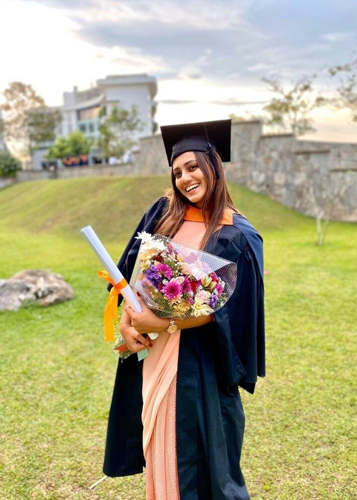 a woman wearing a graduation gown and holding flowers