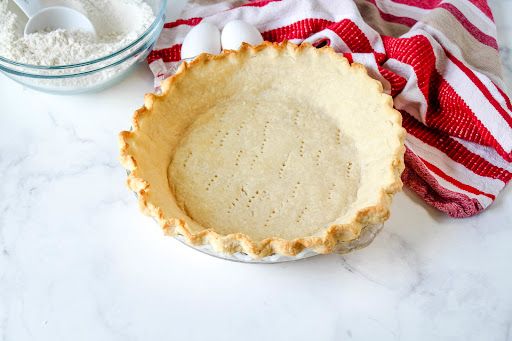 an uncooked pie crust in a bowl next to two measuring cups on a marble countertop