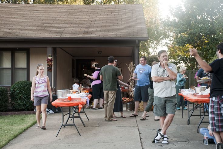 a group of people standing in front of a house next to an orange table with food on it