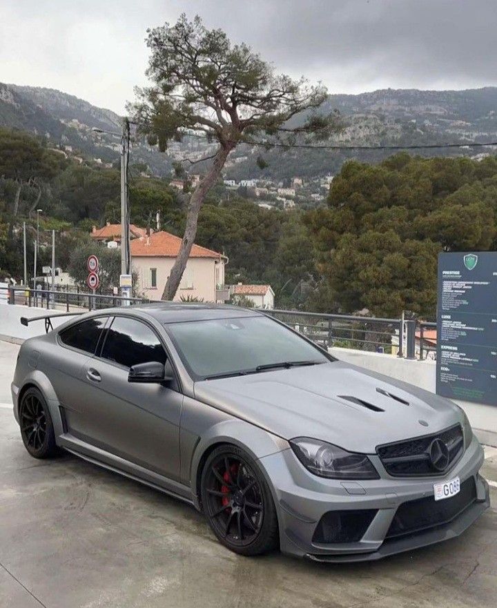 a silver car parked on top of a cement parking lot next to a forest covered hillside