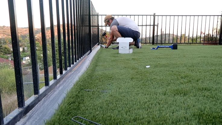 a man kneeling down on top of a lush green field next to a metal fence