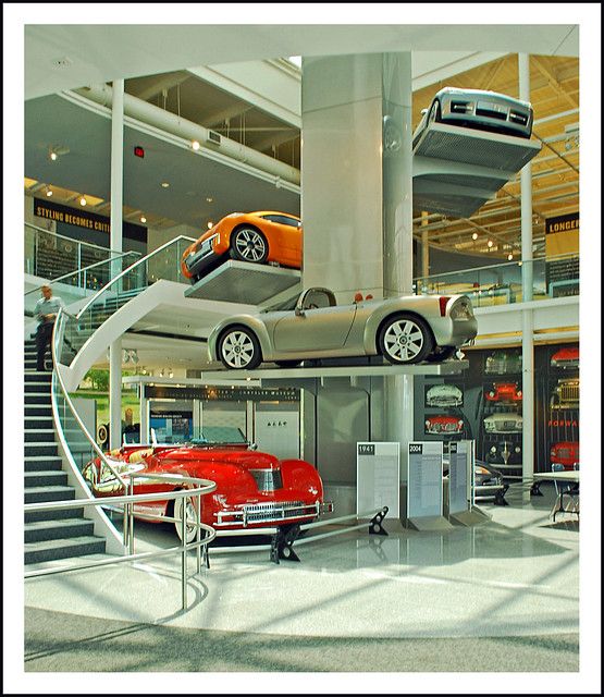 two cars are parked on top of each other in a car showroom with stairs leading up to the second floor