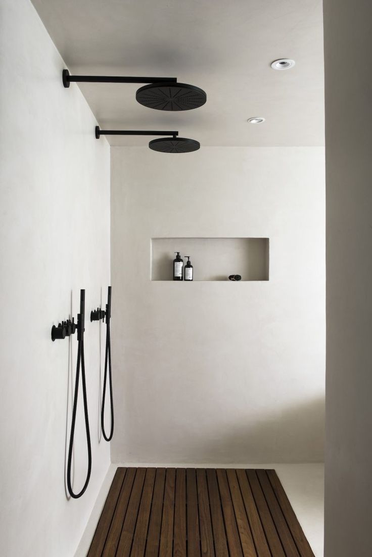 a white bathroom with wooden flooring and black shower faucets on the wall