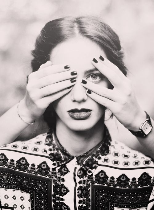 black and white photograph of a woman covering her eyes with both hands while looking at the camera