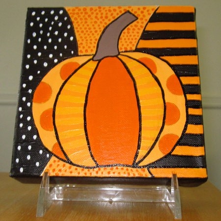 an orange pumpkin painted on a black and white striped background with polka dots, sitting on a clear acrylic stand