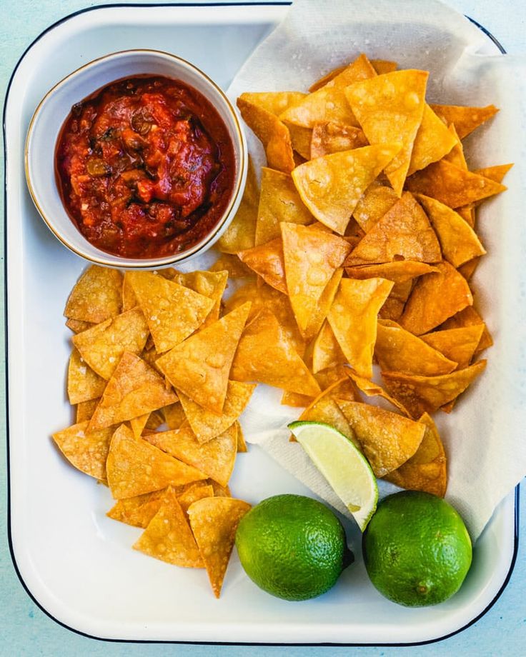 a white plate topped with chips and salsa next to limes on a blue table