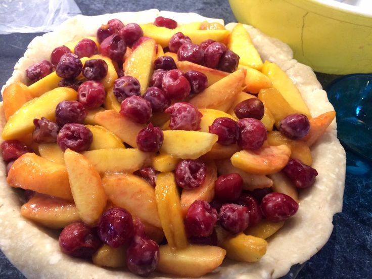 a pie with cranberries and peaches on it next to a yellow bowl