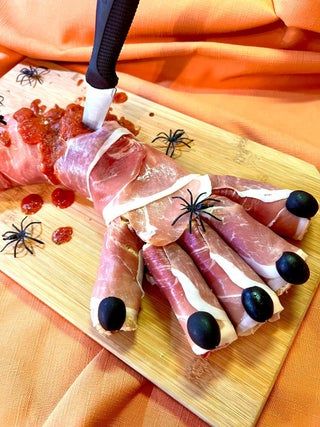 several different types of meat on a cutting board with a knife and spider decorations around it