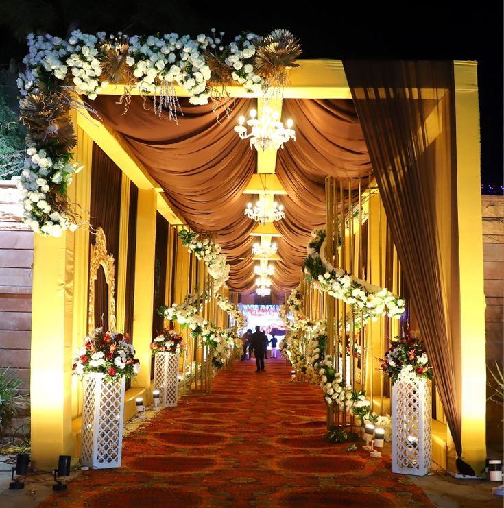 a long hallway decorated with white flowers and chandeliers for an outdoor wedding ceremony