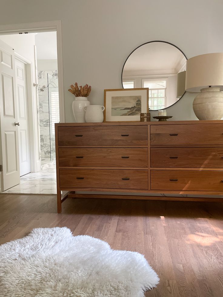 a large white rug on top of a wooden dresser next to a mirror and lamp