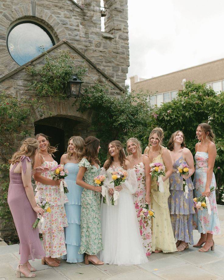 a group of women standing next to each other in front of a stone building holding bouquets