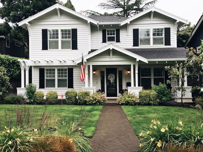 a white house with black shutters and an american flag on the front door is shown