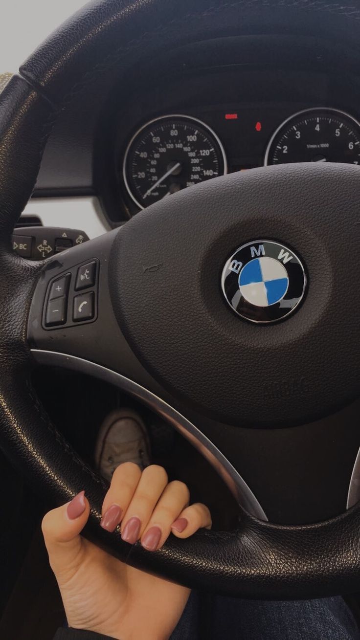 a woman driving a bmw car with her hands on the steering wheel, while she is holding