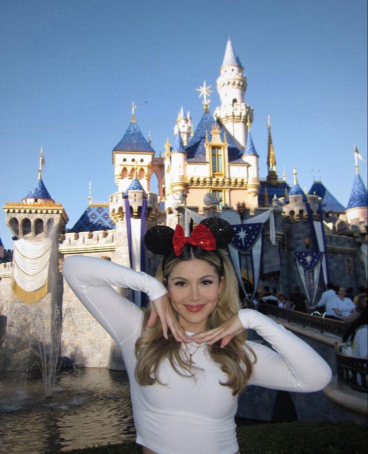 a woman posing in front of a castle with a minnie mouse ears on her head