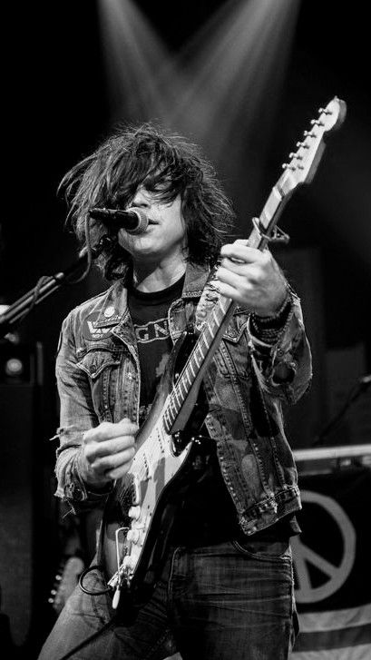 a man with long hair playing an electric guitar in front of microphones and lights