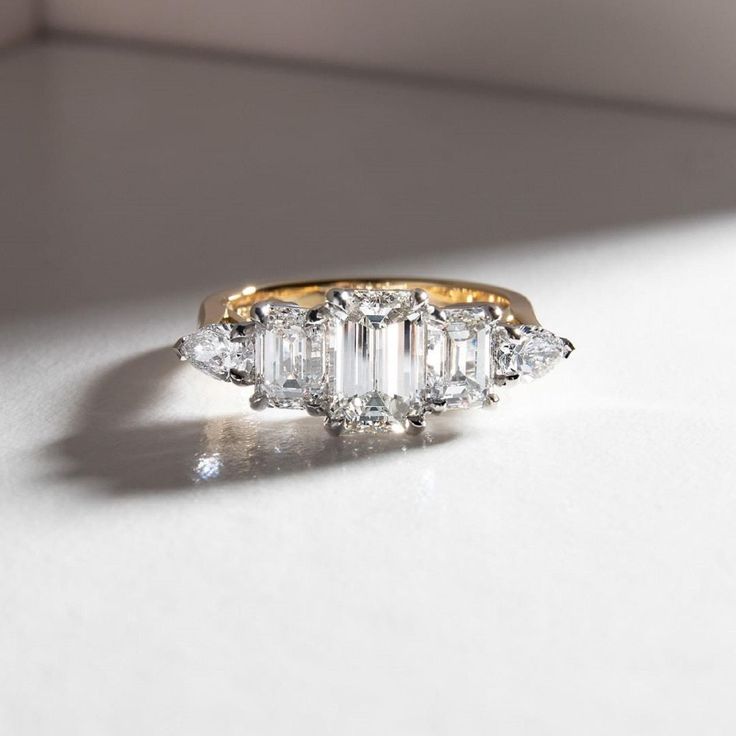 three stone diamond ring sitting on top of a white surface with sunlight coming through the window