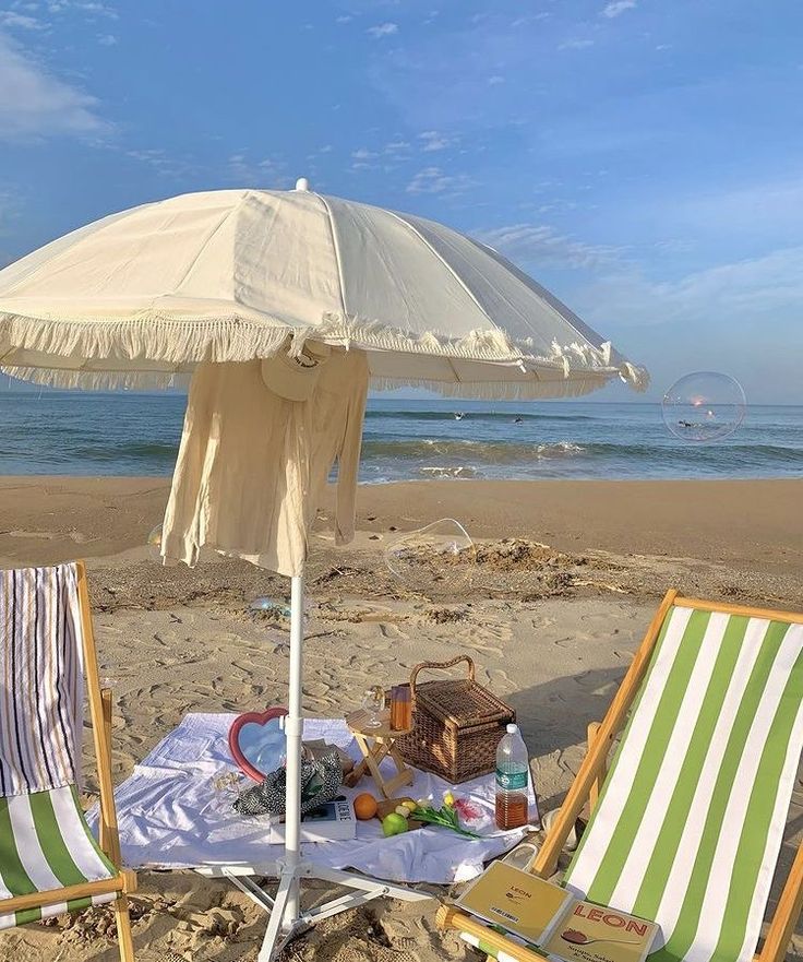 two lawn chairs and an umbrella are on the sand at the beach near the ocean