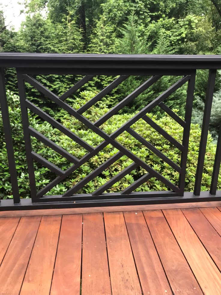 a wooden deck with black iron railings and green bushes on the other side, in front of a wooded area