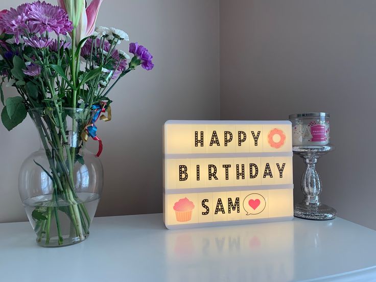 a vase with flowers sitting next to a sign that says happy birthday sam