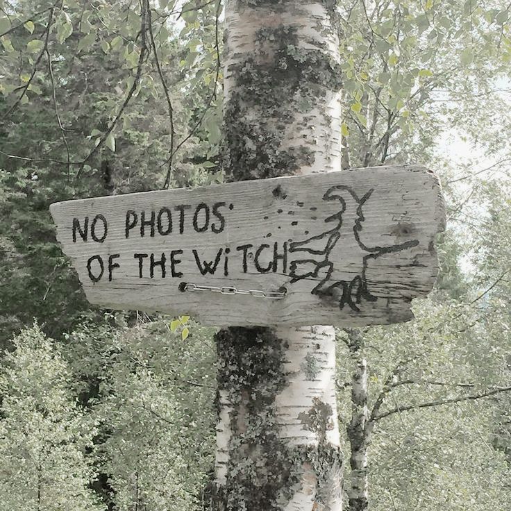 a wooden sign that says no photos of the witch on it next to a tree