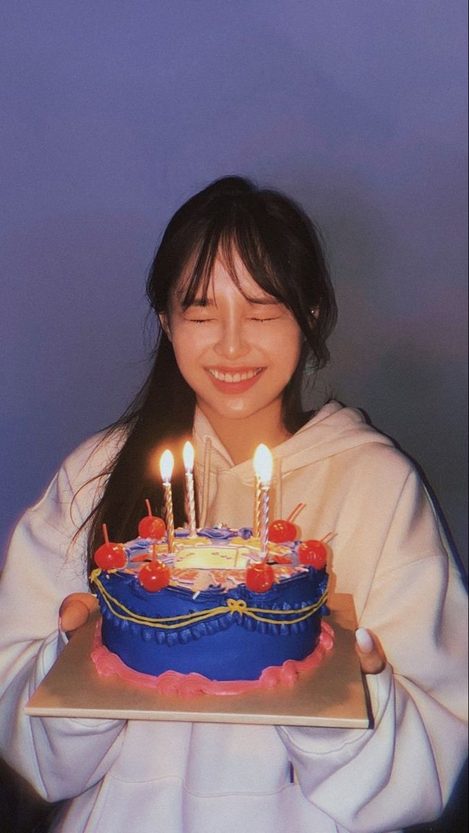 a woman holding a birthday cake with lit candles on it in front of her face