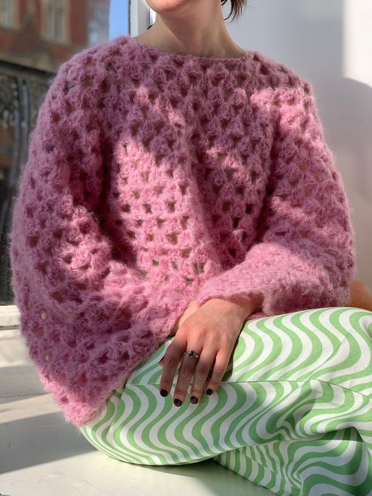 a woman sitting on a window sill wearing a pink sweater