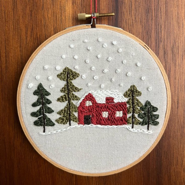 a red house in the snow surrounded by pine trees on a wooden surface with a hook