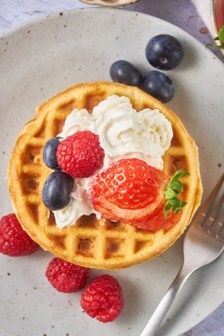 a waffle topped with whipped cream and fresh berries on a plate next to a fork