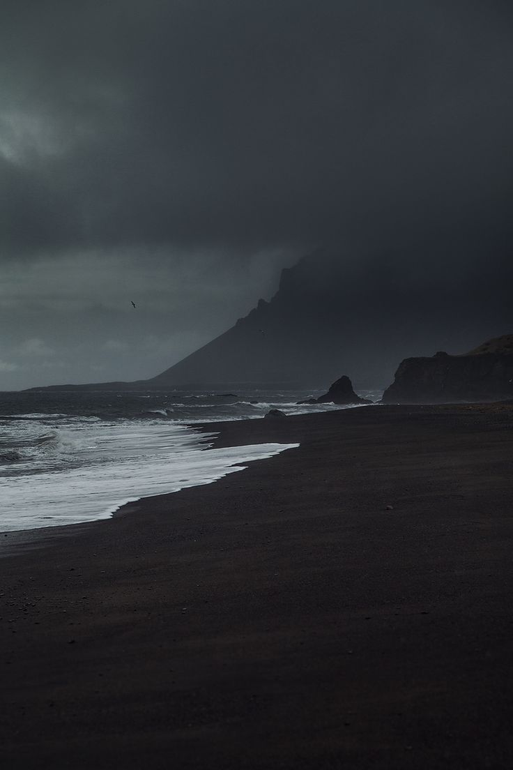 a black and white photo of the ocean with dark clouds in the sky above it