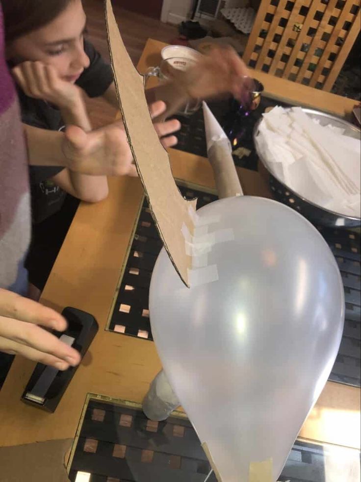 two people cutting up a heart shaped balloon on a table with other items in the background