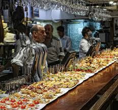 a long table filled with lots of food on top of a wooden counter next to wine glasses