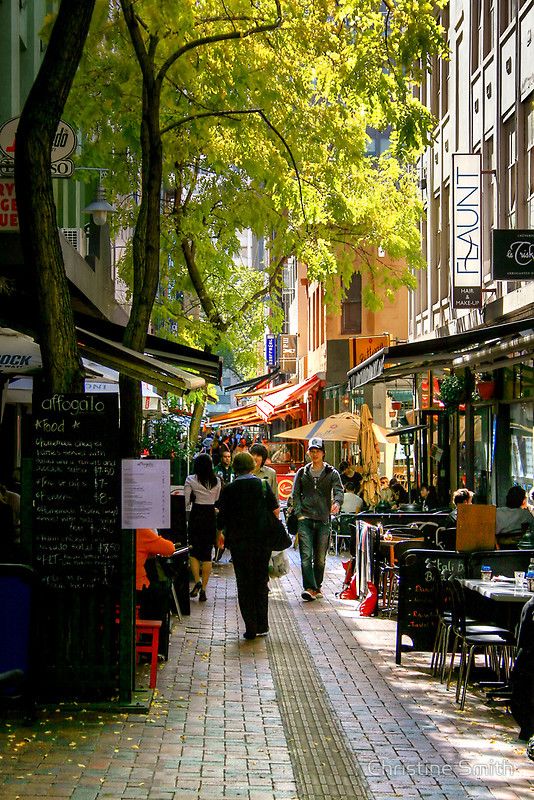 people are walking down the sidewalk in front of shops and restaurants on a sunny day