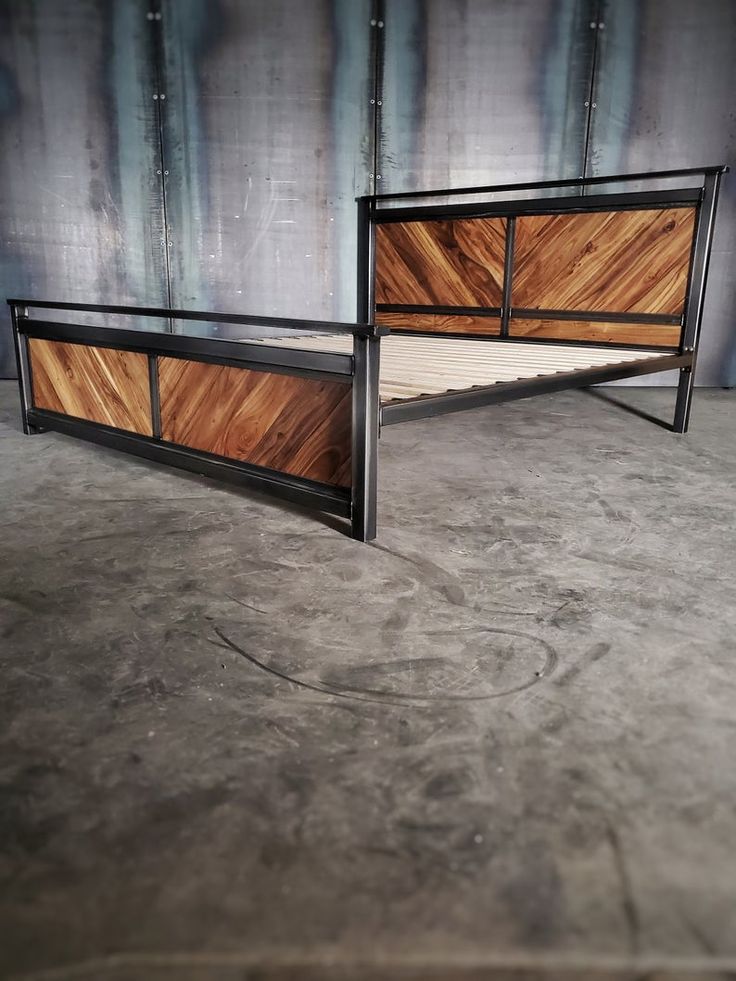 two wooden and metal beds side by side on concrete floor with wall in the background