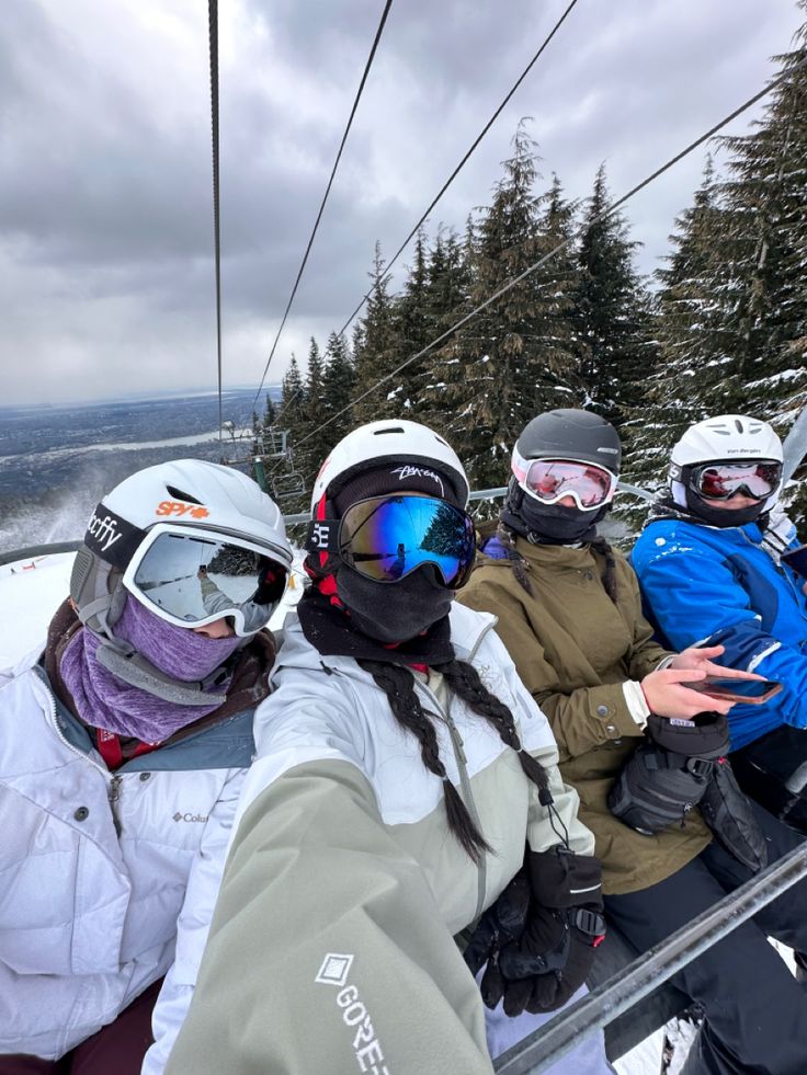 four people sitting on a ski lift with snow covered trees in the backgroud