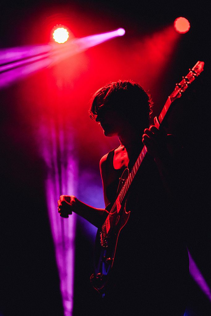 a man playing guitar on stage with red and purple lights in the backround