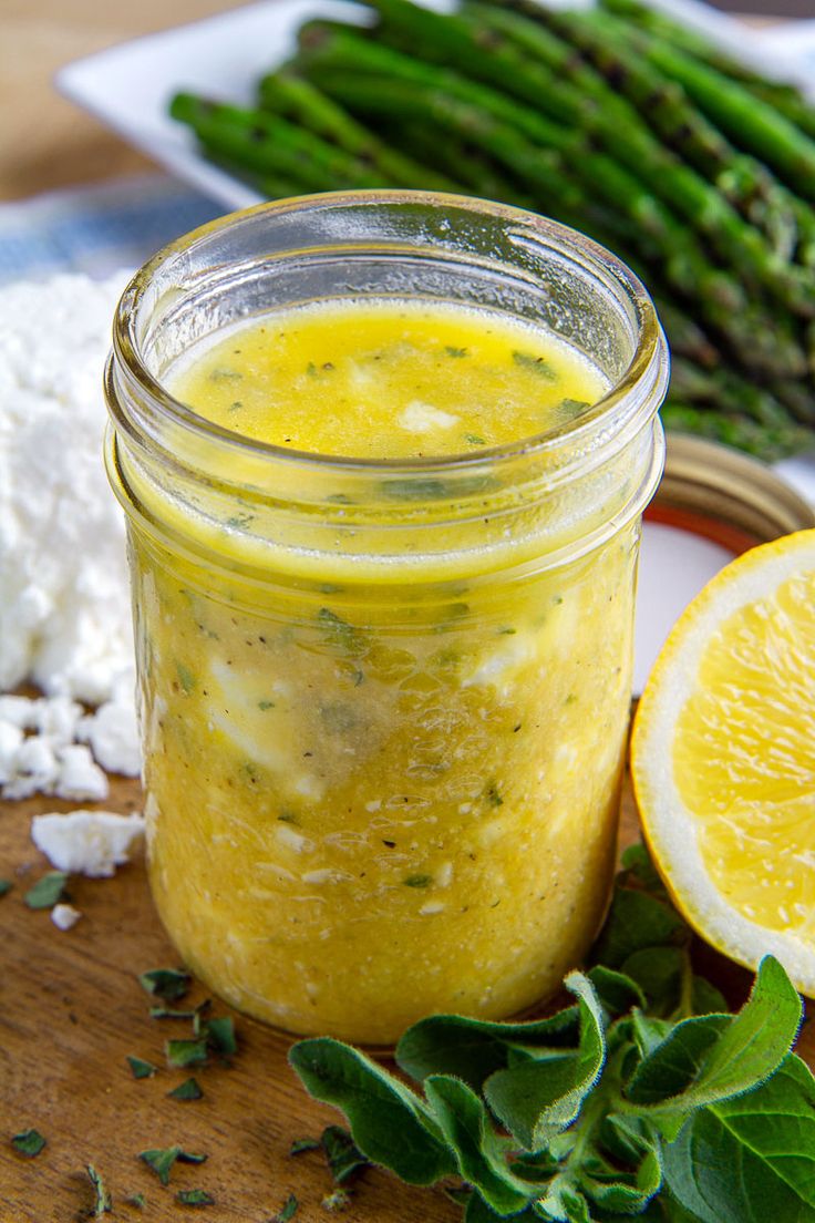 a jar filled with yellow liquid sitting on top of a wooden cutting board next to asparagus