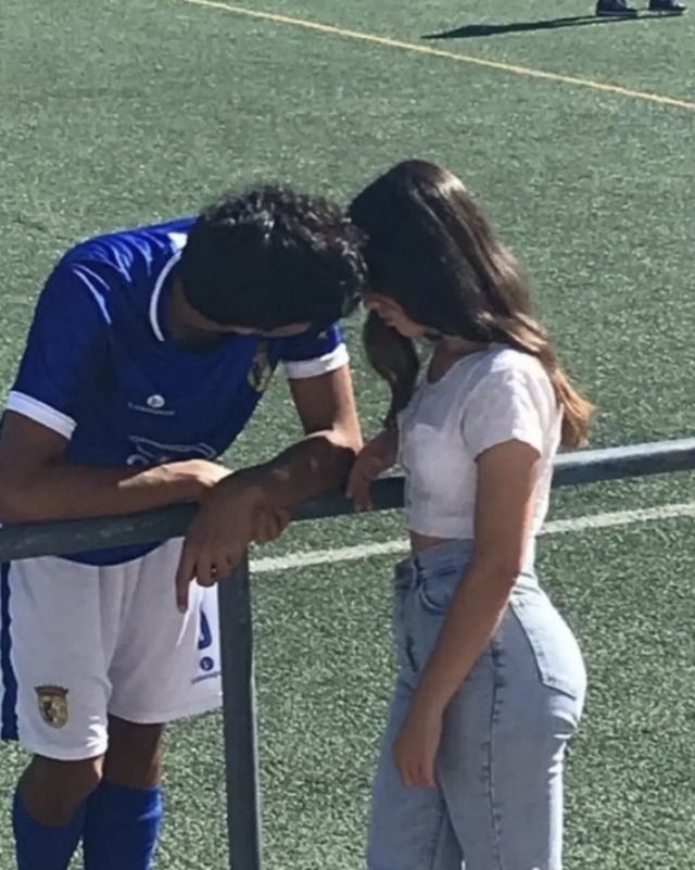 a man and woman standing next to each other near a fence on a soccer field