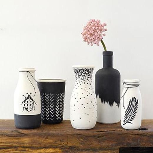 four vases with flowers in them are sitting on a wooden table and one is painted black and white