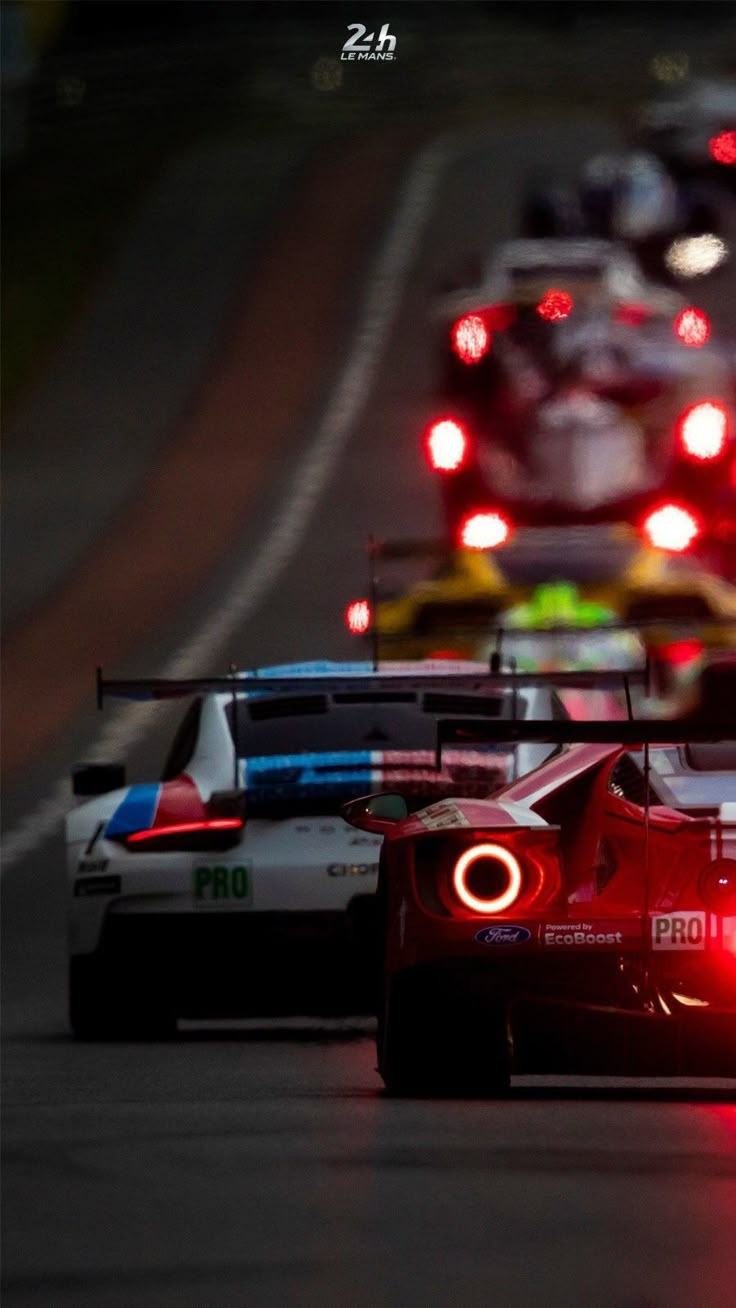 a group of cars driving down a race track with lights on the side of them